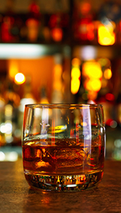 Glass tumbler with bourbon in front of a bar.